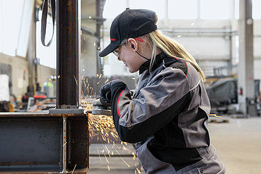 Lehre Metallbauer:in Metallbau-Lernende arbeitet mit, unter Funken sprühenden Winkelschleifer.