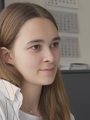 Junge KV-Lernende mit hellbrauen Haaren und einem leichtem Lächeln mit Blick zum Monitor