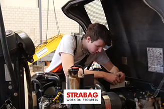 Junger STRABAG Lernender (Maschinist) beim Prüfen eines Baumaschinenmotors.