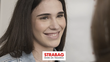 KV-Lernende mit dunklen Haaren und einem strahlendem Lächeln gegenüber einer anderen Person