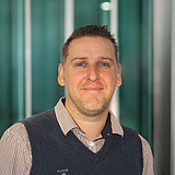 STRAGAB Ausbildungskoordinator KV schaut lächelnd in die Kamera. Er ist mit einer Weste und Hemd gekleidet. Im Hintergrund ist ein Lift zusehen.