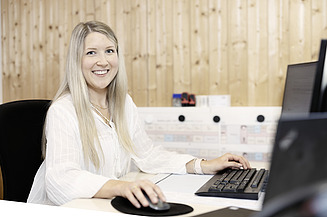 STRABAG KV-Lernende (Kauffrau) am IT-Arbeitsplatz mit lächeldem Blick in die Kamera